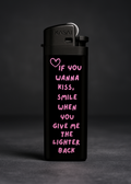 Parmaklar arasında yakılırken görünen siyah çakmak, üzerinde pembe kalp sembolü ve “If you wanna kiss” yazılı tasarım metni bulunan banner görseli.